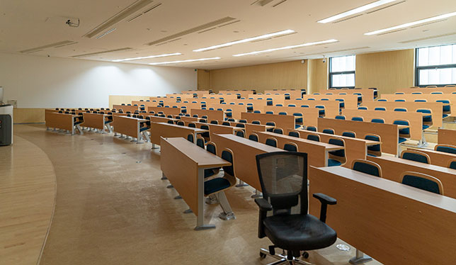 A single desk chair sits in the foreground of an empty lecture hall.